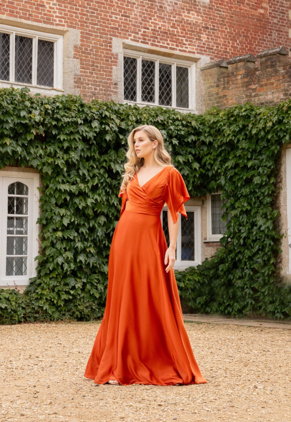 A bridesmaid in a rust flutter-sleeve gown outside a country house