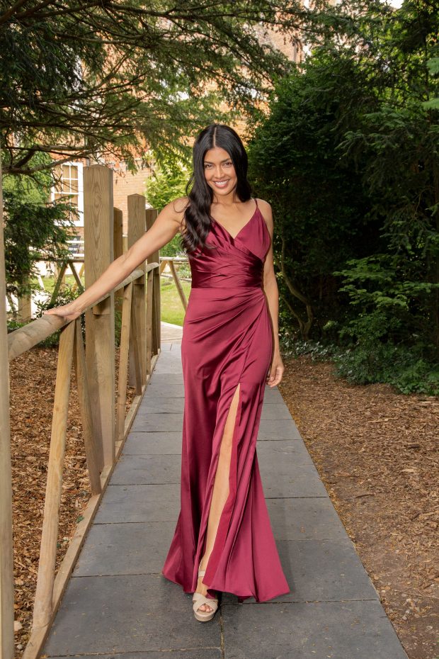 A bridesmaid in a berry-red satin gown with a ruched wrap bodice and a thigh split
