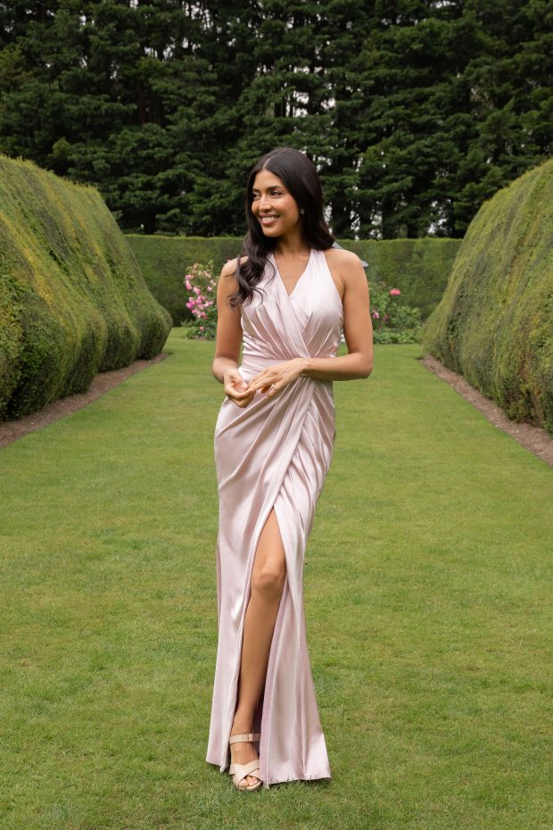 A bridesmaid in an oyster-pink halter-neck satin gown with a draped wrap skirt