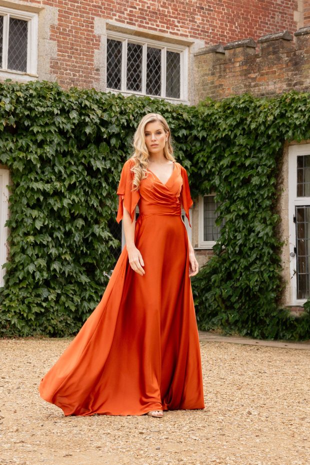 A bridesmaid in a rust satin gown with flutter sleeves and a sweeping skirt