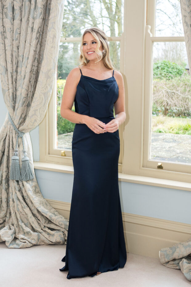 A bridesmaid in a navy satin cowl-neck gown with fine straps